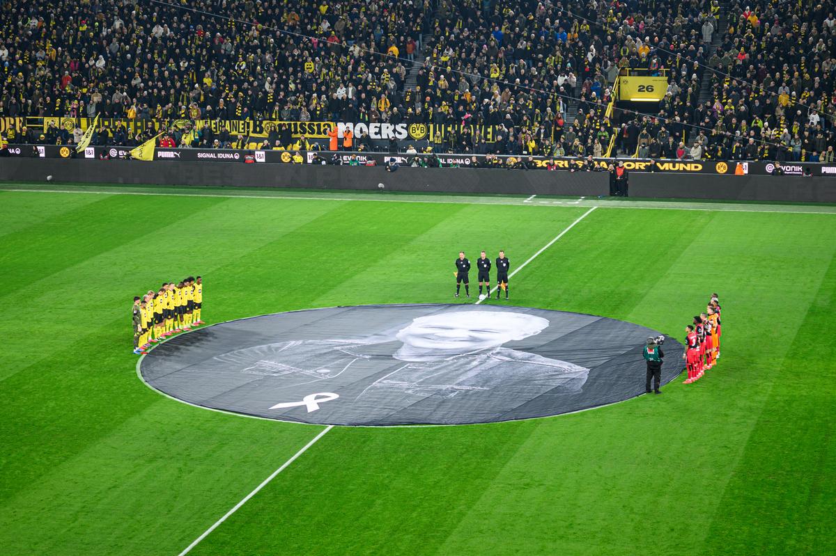Người hâm mộ và các cầu thủ Borussia Dortmund bày tỏ lòng kính trọng đối với huyền thoại Wolfgang 'Teddy' de Beer, người đã qua đời vào tháng 12, ngay trước trận đấu với Bayer Leverkusen tại sân vận động Signal Iduna Park. Người hâm mộ và các cầu thủ Borussia Dortmund bày tỏ lòng kính trọng đối với huyền thoại Wolfgang 'Teddy' de Beer, người đã qua đời vào tháng 12, ngay trước trận đấu với Bayer Leverkusen tại sân vận động Signal Iduna Park.